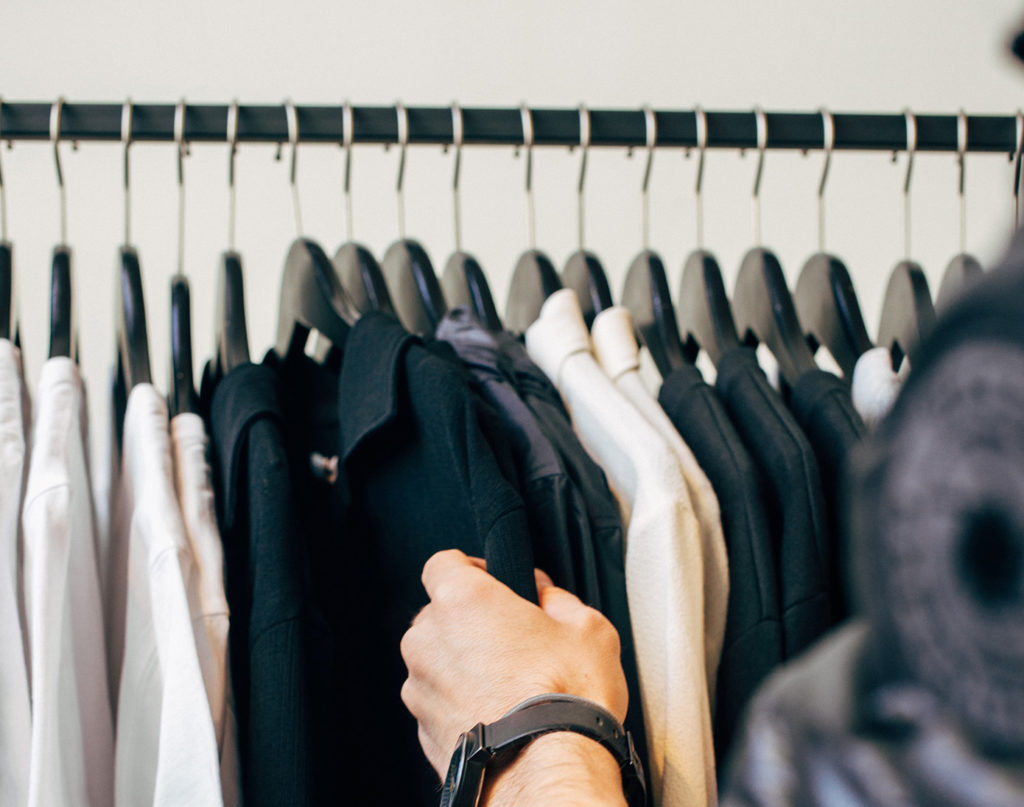 Person touching a shirt displayed on a clothing rack. Photo by Charles Deluvio, Unsplash.